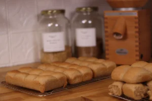 fresh milled flour dinner rolls on a cooling rack with a grain mill in the background